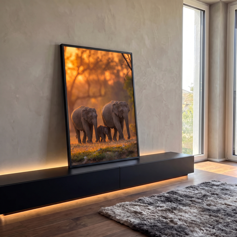 Dois elefantes e filhote caminhando em floresta sob luz laranja do pôr do sol, quadro decorativo