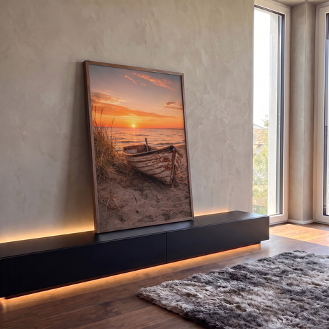 Barco de madeira envelhecido na areia com capim de duna e pôr do sol laranja sobre o mar, quadro decorativo