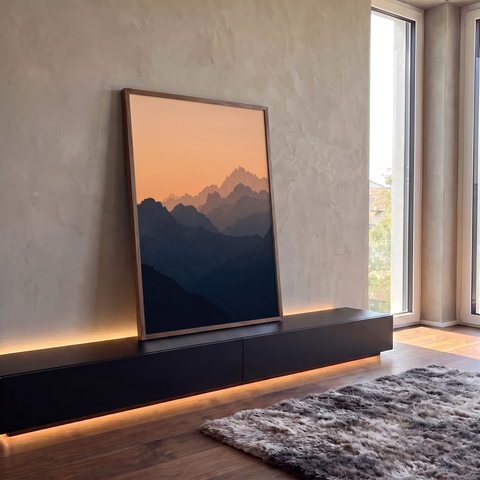 Silhuetas de montanhas em camadas azuladas sob céu laranja de entardecer, paisagem vertical, quadro decorativo