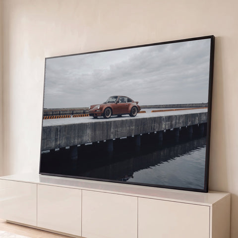 Porsche 911 clássico cor cobre em píer de concreto sobre o mar sob céu cinza, quadro decorativo