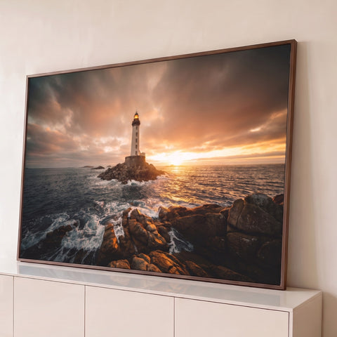 Farol branco sobre rochas no mar com ondas e céu laranja ao pôr do sol, quadro decorativo