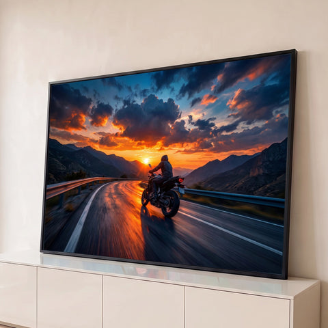 Motociclista fazendo curva em estrada de montanha ao pôr do sol com céu laranja e nuvens, quadro decorativo