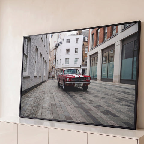 Mustang clássico vermelho com faixas brancas em rua de paralelepípedos entre prédios antigos, quadro decorativo