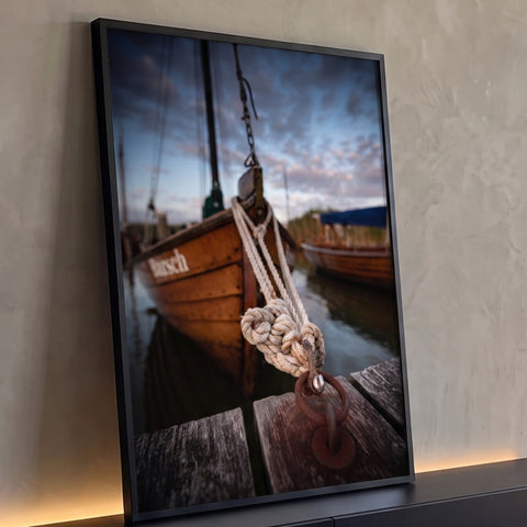 Nó de corda em argola de ferro no cais de madeira com barcos ao entardecer, quadro decorativo