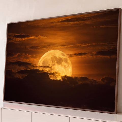Superlua dourada com crateras nascendo atrás de nuvens escuras em céu laranja de entardecer, quadro decorativo