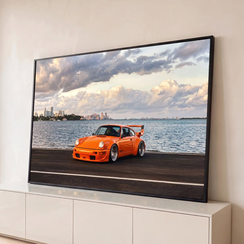 Porsche 911 laranja com aerofólio na orla, mar e skyline sob nuvens ao entardecer, quadro decorativo