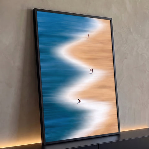 Praia vista do alto com mar azul, espuma branca em zigue-zague e pessoas na areia, quadro decorativo