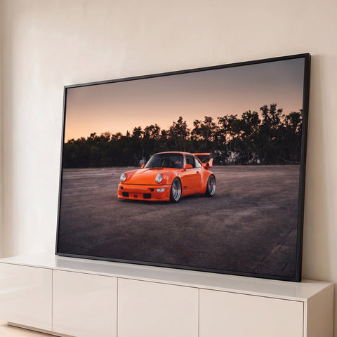 Porsche 911 RWB laranja com aerofólio em pátio de asfalto ao entardecer, árvores ao fundo, quadro decorativo