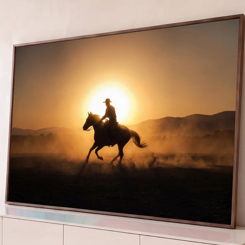 Silhueta de cowboy galopando a cavalo em contraluz ao pôr do sol com poeira dourada, quadro decorativo