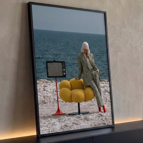 Mulher de terno xadrez e cabelo platinado com poltrona amarela e TV retrô à beira-mar, quadro decorativo