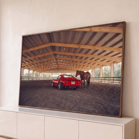 Ferrari clássica vermelha ao lado de cavalo marrom em picadeiro coberto de haras, quadro decorativo