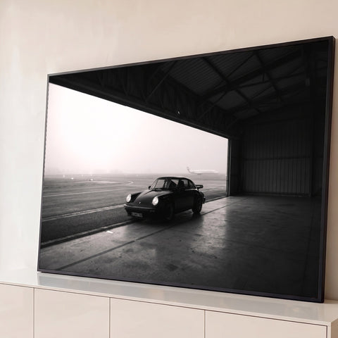 Porsche 911 clássico parado em hangar com avião na pista sob neblina, foto preto e branco, quadro decorativo