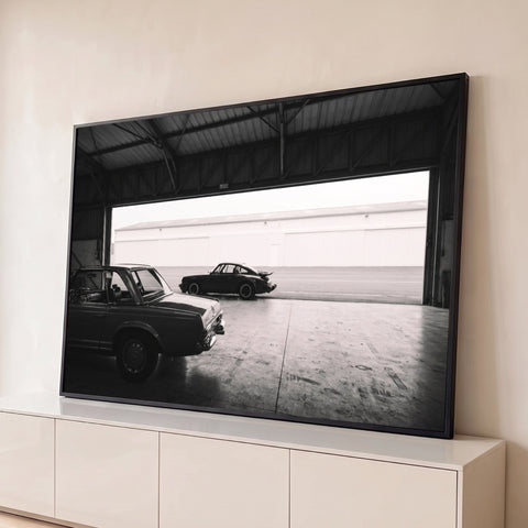 Porsche 911 e Mercedes clássicos em hangar industrial, fotografia preto e branco, quadro decorativo