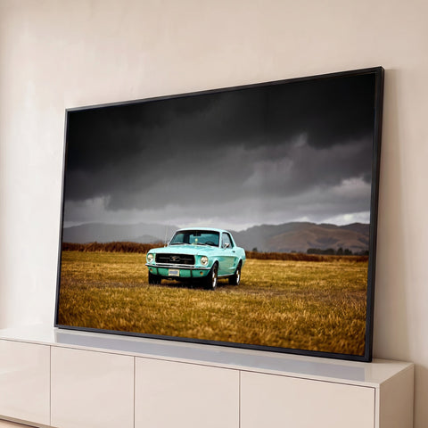 Mustang clássico turquesa em campo dourado sob céu cinza de tempestade e montanhas, quadro decorativo