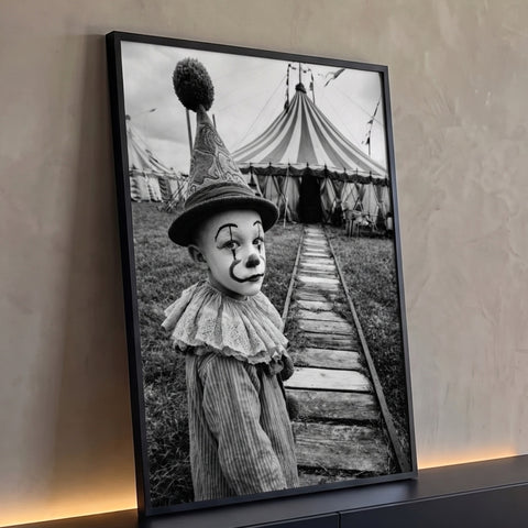 Menino vestido de palhaço com gola de renda diante de tenda de circo em preto e branco, quadro decorativo