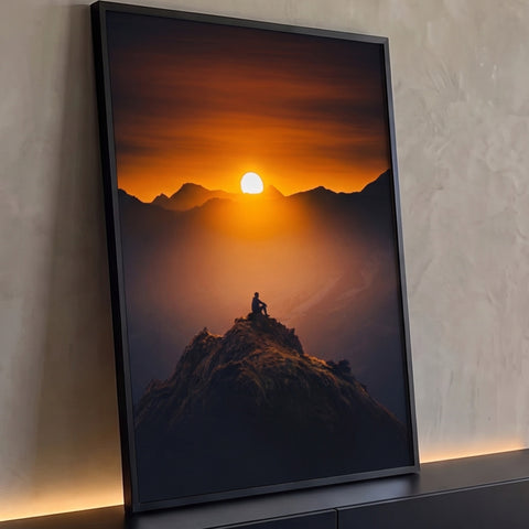 Silhueta de pessoa sentada no pico da montanha diante do pôr do sol laranja, quadro decorativo