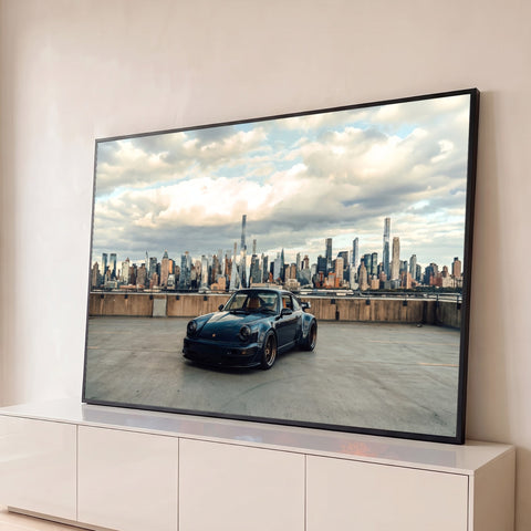 Porsche 911 azul-escuro em terraço com skyline de Nova York e céu nublado ao fundo, quadro decorativo