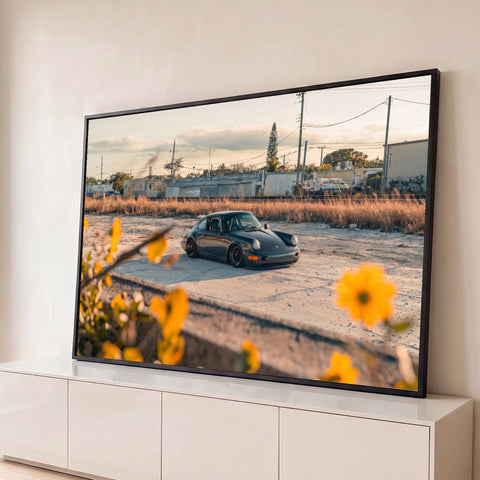 Porsche 911 clássico rebaixado ao entardecer com flores amarelas em primeiro plano, quadro decorativo