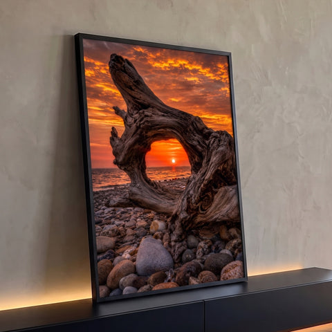 Sol se pondo no mar emoldurado por arco de tronco seco sobre praia de seixos e céu laranja, quadro decorativo