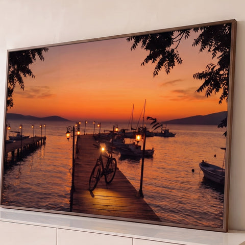 Bicicleta em píer de madeira com lampiões acesos e barcos no mar ao pôr do sol laranja, quadro decorativo