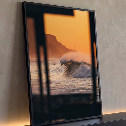 Onda gigante quebrando no mar ao pôr do sol laranja com falésia, vista de janela escura, quadro decorativo