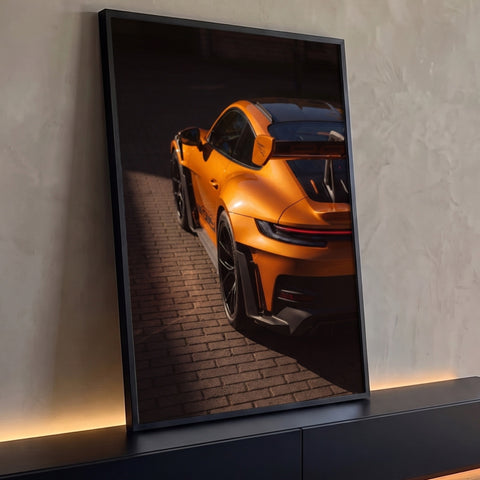 Porsche GT3 RS laranja visto de trás com aerofólio, luz do sol e piso de tijolos, quadro decorativo