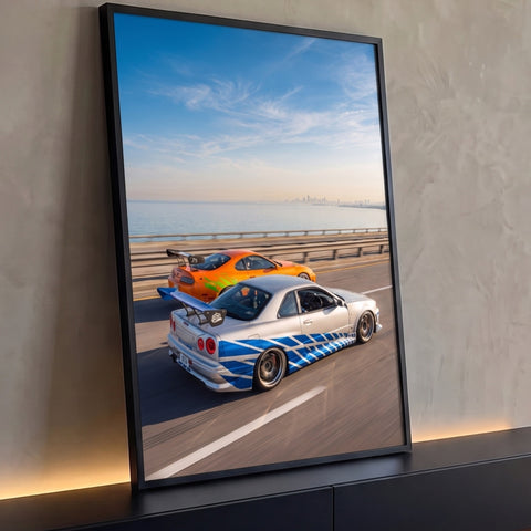 Carro prata com faixas azuis e carro laranja correndo em ponte à beira-mar sob céu azul, quadro decorativo