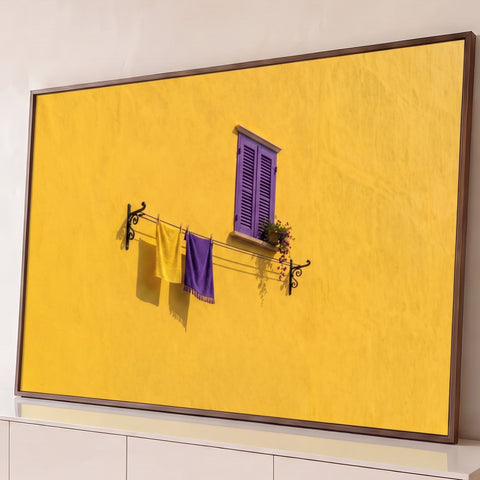 Parede amarela com janela de venezianas roxas, flores e varal com toalhas amarela e roxa, quadro decorativo