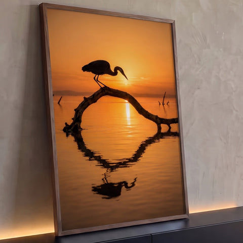 Garça em silhueta sobre galho arqueado no lago ao pôr do sol laranja com reflexo, quadro decorativo