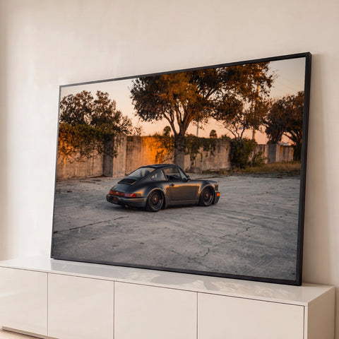 Porsche 911 clássico cinza rebaixado com rodas bronze em pátio de concreto ao entardecer, quadro decorativo