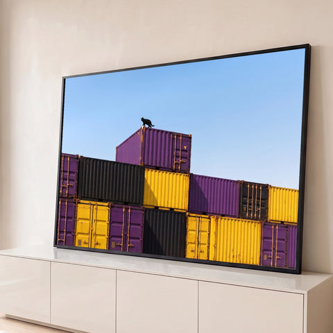 Gato preto caminhando sobre contêineres roxos, amarelos e pretos sob céu azul, quadro decorativo