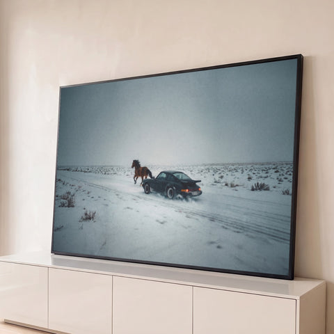 Porsche clássico preto e cavalo marrom correndo lado a lado em estrada com neve e céu cinza, quadro decorativo