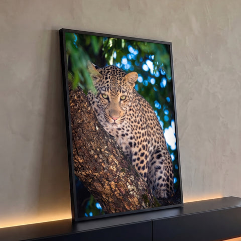Leopardo apoiado em tronco de árvore com olhos verdes e fundo de folhagem com bokeh, quadro decorativo