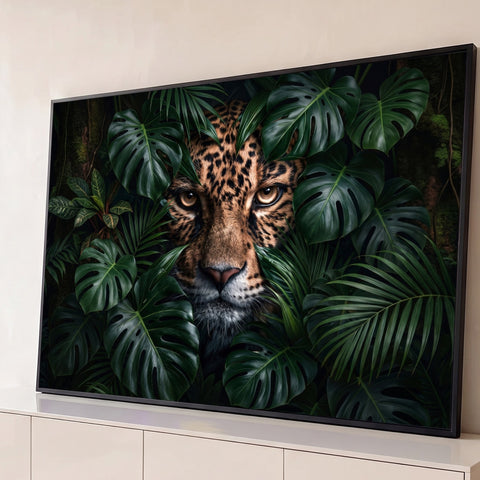 Rosto de onça-pintada com olhos âmbar espreitando entre folhas de monstera e palmeiras, quadro decorativo