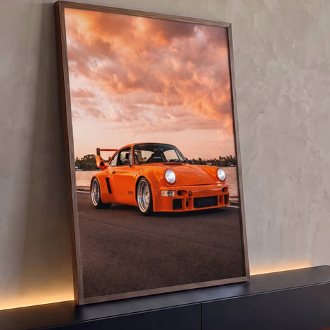 Porsche 911 widebody laranja em estrada à beira-mar sob céu de pôr do sol, quadro decorativo