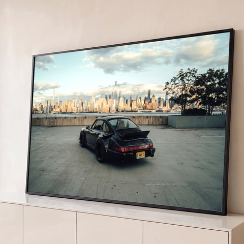 Porsche 911 preto com aerofólio em terraço de concreto e skyline de Nova York ao entardecer, quadro decorativo