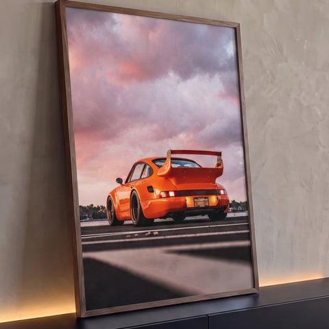 Porsche 911 laranja com aerofólio visto de trás na pista sob céu rosa de pôr do sol, quadro decorativo