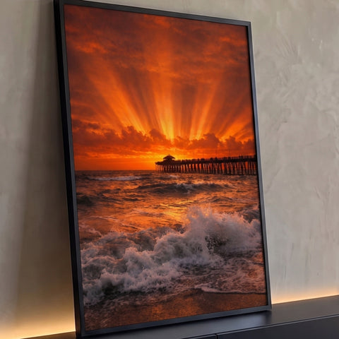 Pôr do sol laranja com raios de luz no céu, píer de madeira e ondas quebrando na praia, quadro decorativo