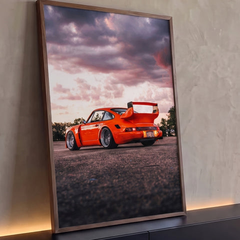 Porsche 911 laranja widebody com aerofólio, vista traseira sob céu rosa ao entardecer, quadro decorativo