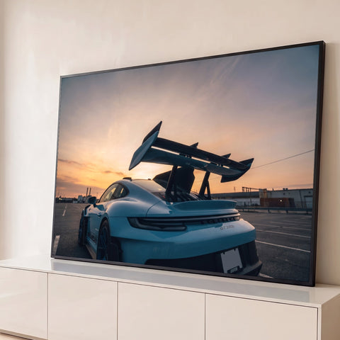 Porsche GT3 RS azul visto de trás com grande aerofólio sob céu de pôr do sol laranja, quadro decorativo