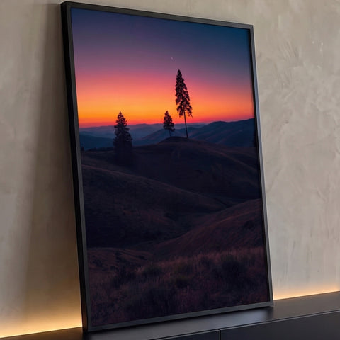 Pinheiros em silhueta sobre colinas escuras ao pôr do sol laranja com lua crescente, quadro decorativo