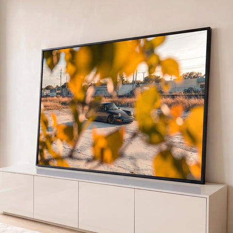 Porsche 911 clássico cinza visto entre folhas amarelas desfocadas ao entardecer, quadro decorativo