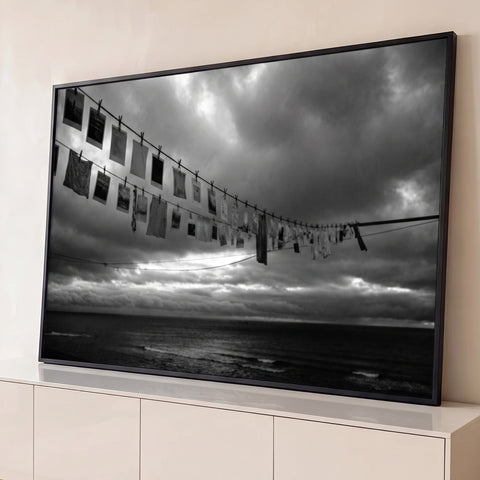 Fotografia preto e branco de varal com fotos antigas e panos sobre o mar sob céu nublado, quadro decorativo