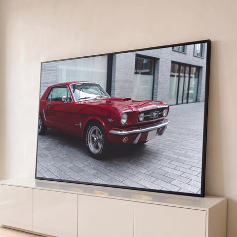 Ford Mustang 1965 vermelho clássico estacionado em rua de pedra diante de prédio moderno, quadro decorativo