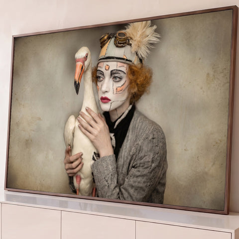 Mulher com maquiagem de boneca e chapéu steampunk abraçando ave branca, fundo bege, quadro decorativo