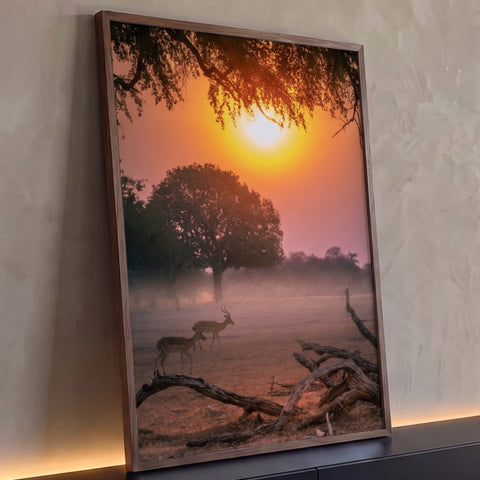 Dois impalas na savana africana ao pôr do sol laranja, com árvore e galhos secos, quadro decorativo