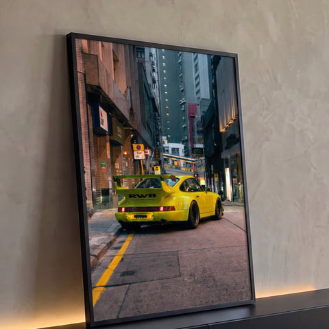 Porsche 911 RWB amarelo rebaixado em rua estreita entre prédios ao entardecer, quadro decorativo