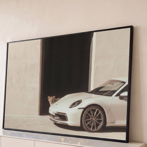 Porsche 911 branco diante de porta escura com filhote de leão espiando, quadro decorativo