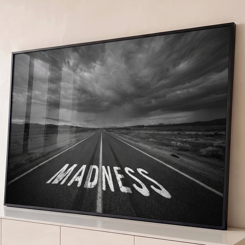 Estrada deserta com a palavra Madness pintada no asfalto sob céu nublado em preto e branco, quadro decorativo