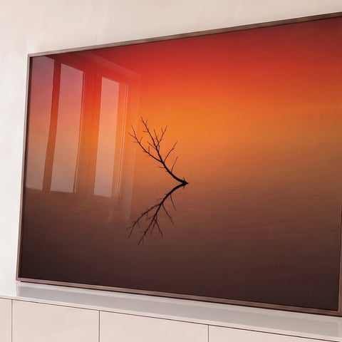 Galho seco refletido em água calma com céu degradê laranja e vermelho ao entardecer, quadro decorativo